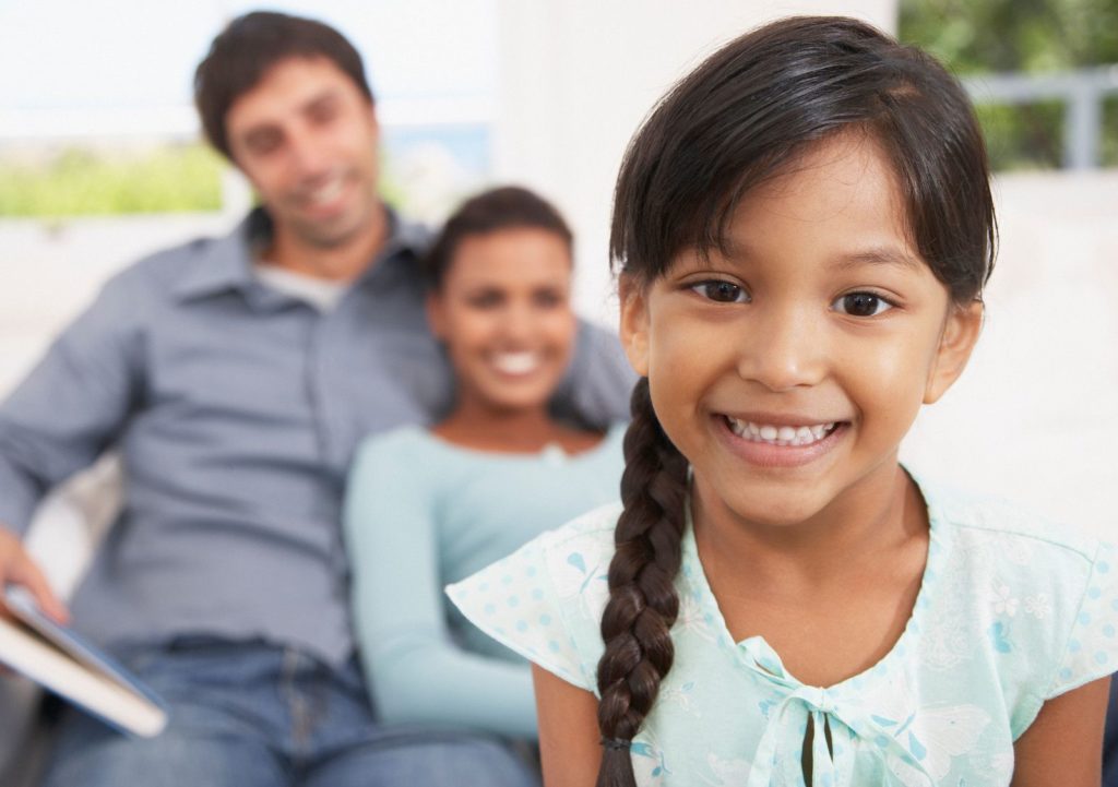 Young girl smiling in front of her family. Psychoeducational and neuropsychological testing can be what your child needs. We offer neuropsychological testing in San Francisco & Berkeley, CA.