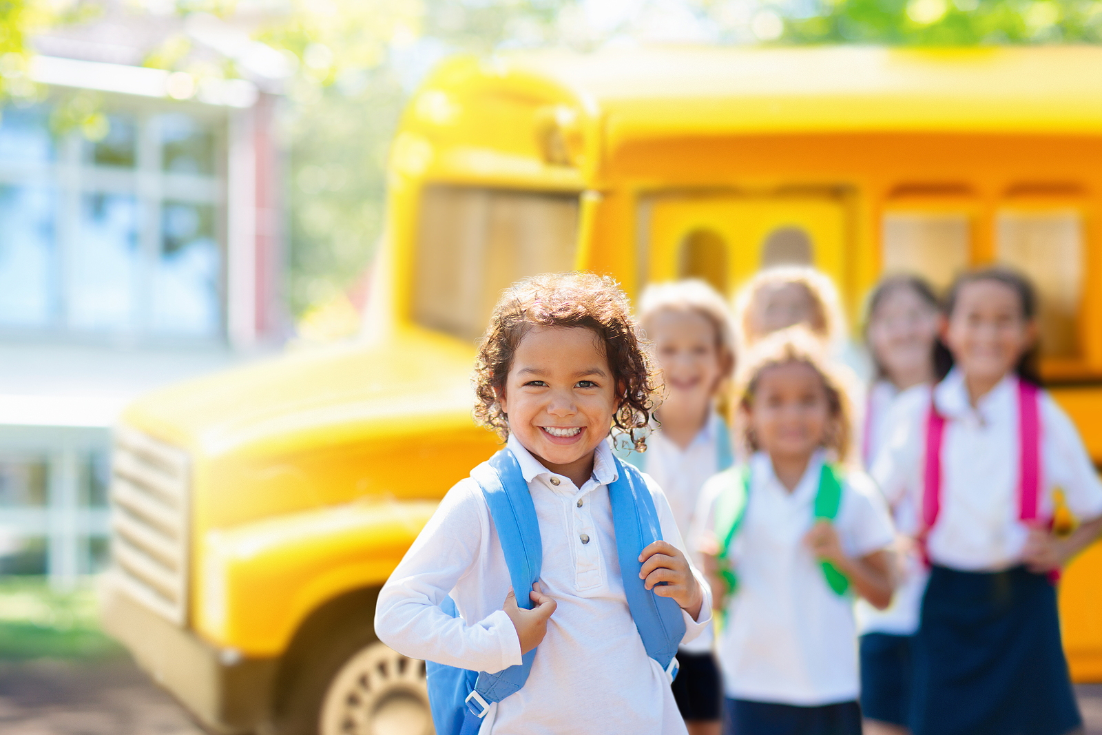 Interracial group of children smiling in front of a school bus. Explore neurodevelopmental screenings in Campbell, CA & dive deeper into autism testing. We also discuss ADHD & dyslexia testing.