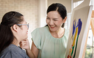 An adult woman smiling at a young adult showing artwork. An autism screening in Berkeley or San Francisco, CA can be your support. Learn more about neurodevelopmental screenings at Mind Matters.