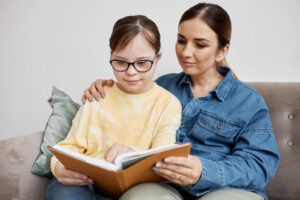 An adult sitting with a young adult reading a book. Dyslexia testing in Berkeley, CA can help your child thrive! Contact our psychologists today to learn more about dyslexia evaluations. 
